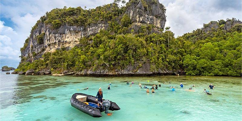 people in water near lush green cliffs