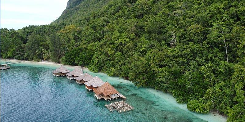 huts floating on water near large green mountain