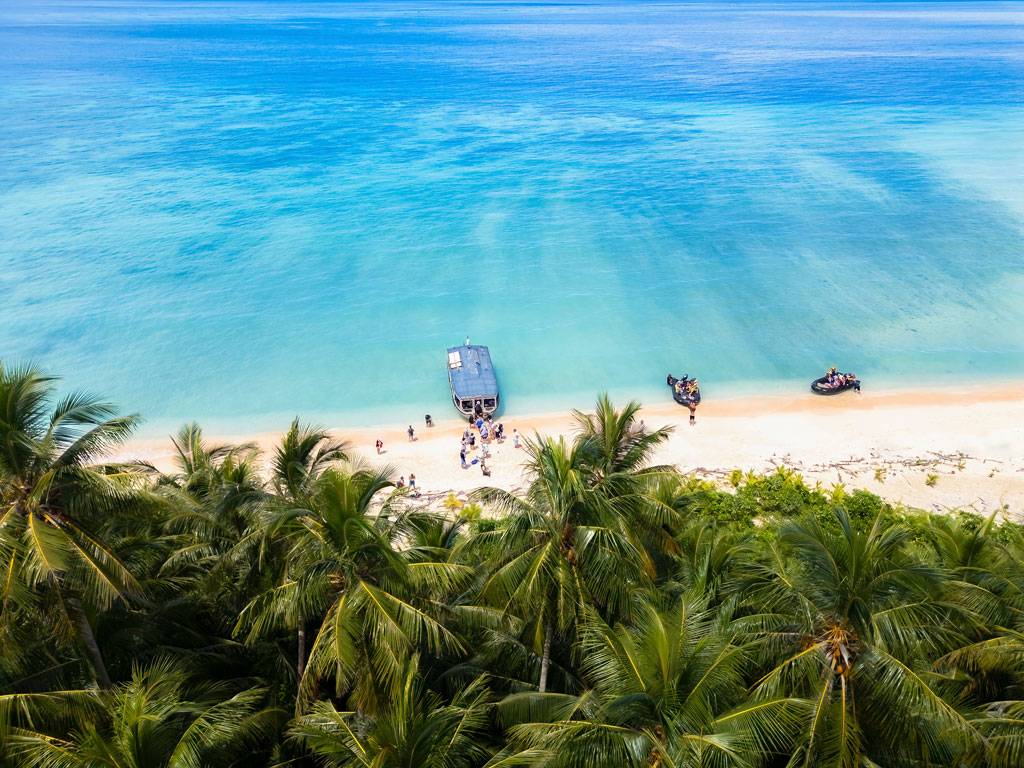Blue water white sand beach with a boat and travellers on it