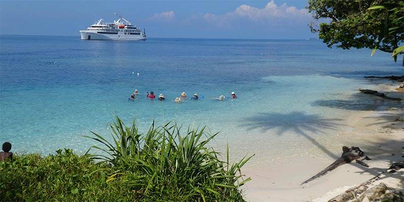large boat at sea with people in shallow water swiming